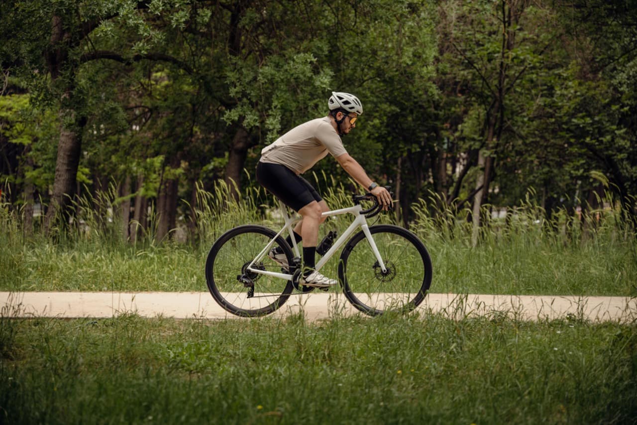 Cycliste en gravel sur un chemin bordé d'herbes et d'arbres