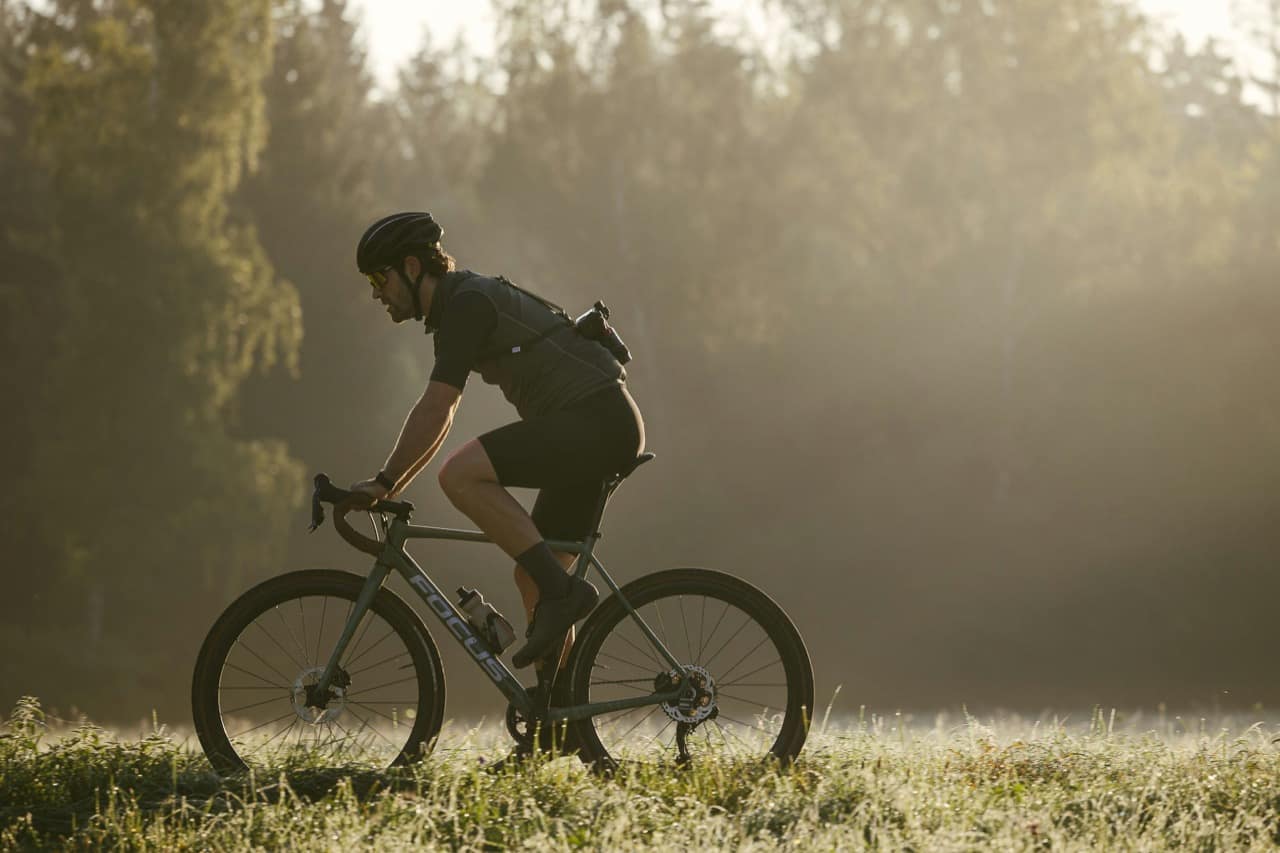 Cycliste en gravel à l'orée d'un bois, dans la lumière du matin